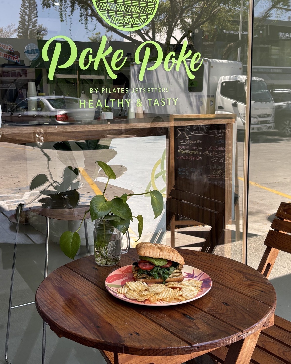 Sándwich servido en una mesa afuera de Jetsetters, frente al ventanal con el letrero "Poke Poke"
