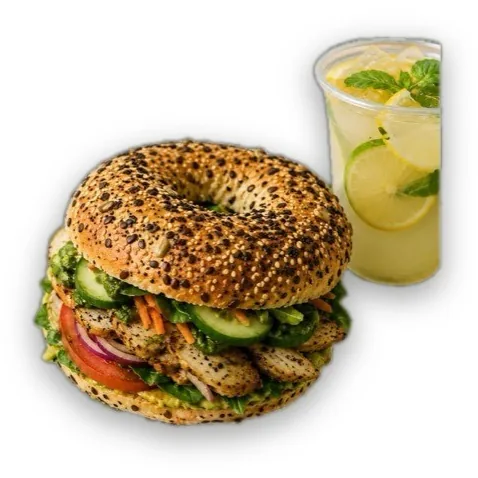 Bagel con semillas relleno de pollo, lechuga, jitomate, cebolla morada y pepino, junto a una bebida cítrica.