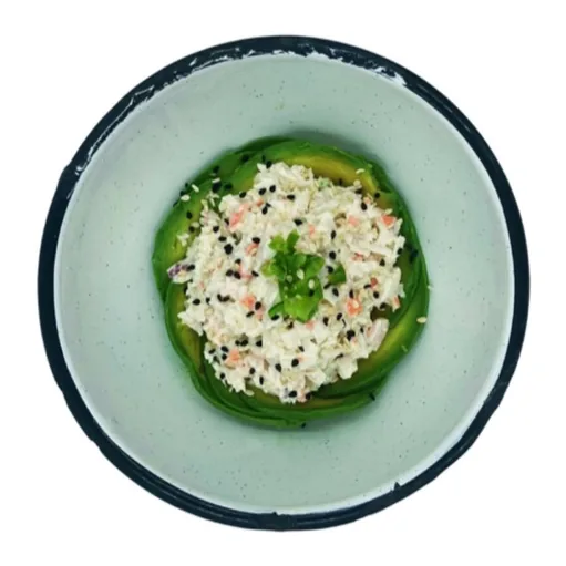 Un dip cremoso y deshebrado, decorado con ajonjolí negro y cebollín, sobre un borde de aguacate.