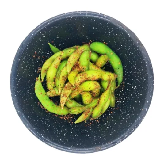 Vainas de edamame sazonadas con un aderezo rojo, en un tazón oscuro moteado.