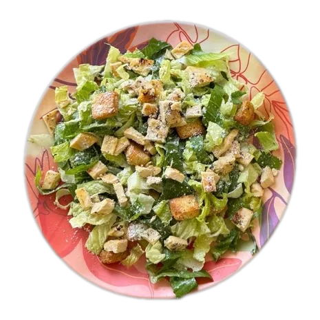 Ensalada César picada con crutones y queso rallado, servida en un plato estampado.