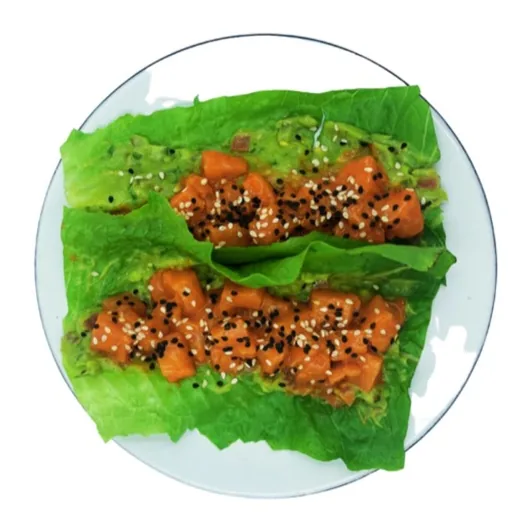 Dos tacos de lechuga rellenos de aguacate machacado y pescado color salmón en cubos, con ajonjolí.