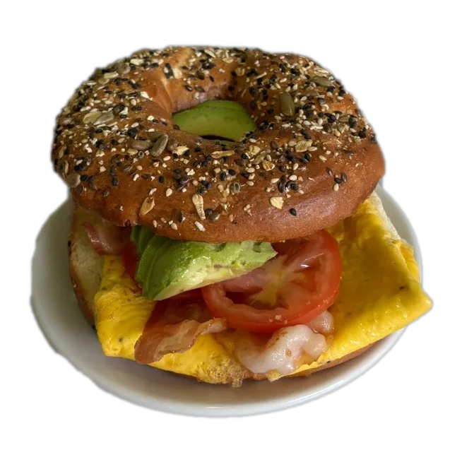 Bagel con semillas relleno de huevo, tocino, jitomate y aguacate, servido en un plato.